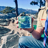 Person holding a bar of soap with a mountainous landscape in the background