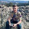 Scout sitting on a rocky outcrop with a scenic background, holding a bar of soap