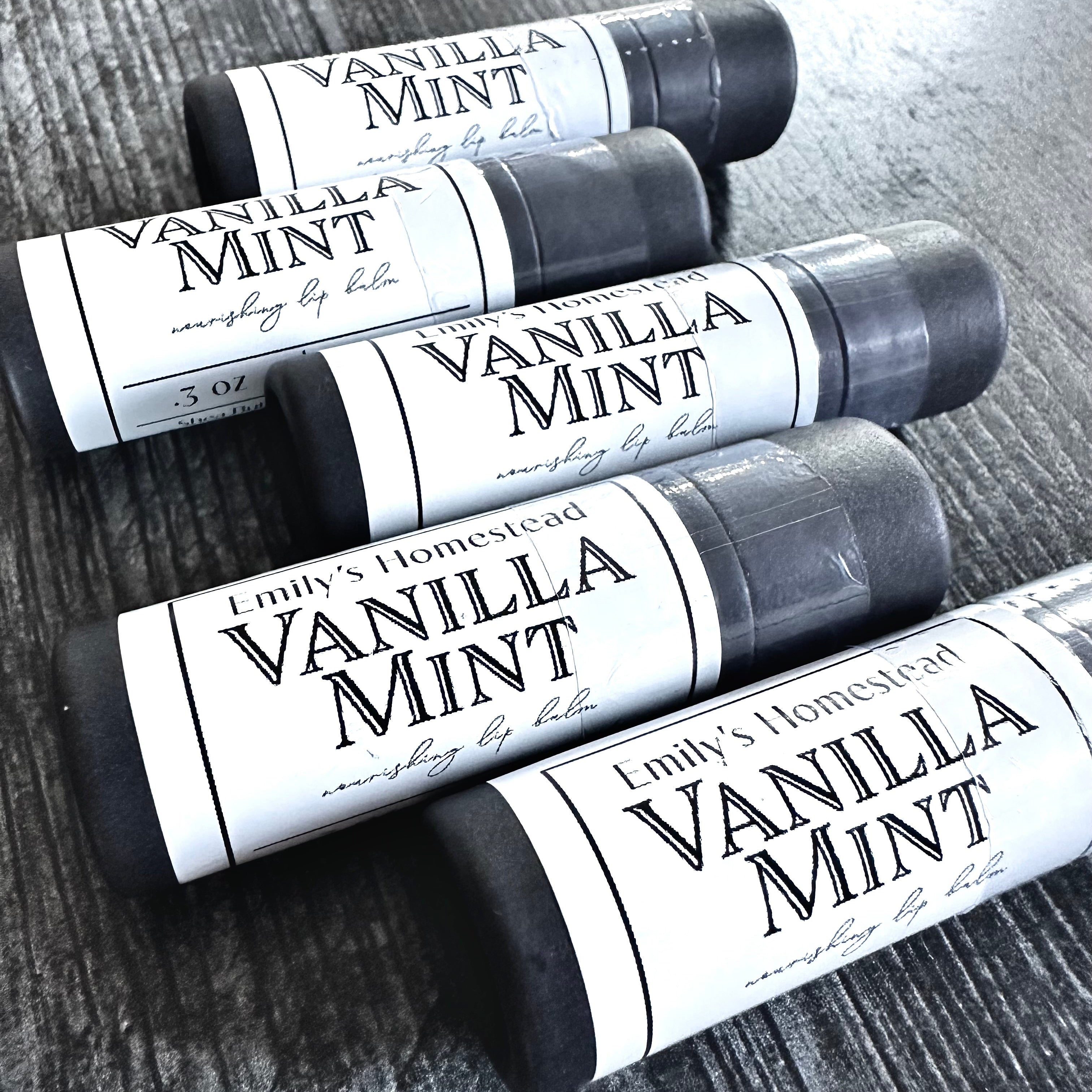 Four lip balm tubes labeled 'Vanilla Mint' on a wooden surface.