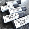 Four lip balm tubes labeled 'Vanilla Mint' on a wooden surface.